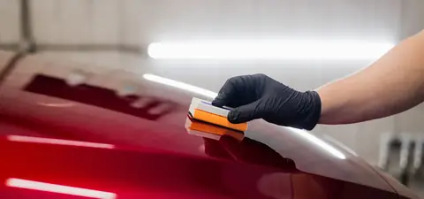 Dłoń w rękawiczce polerująca czerwony lakier ściereczką z mikrofibry